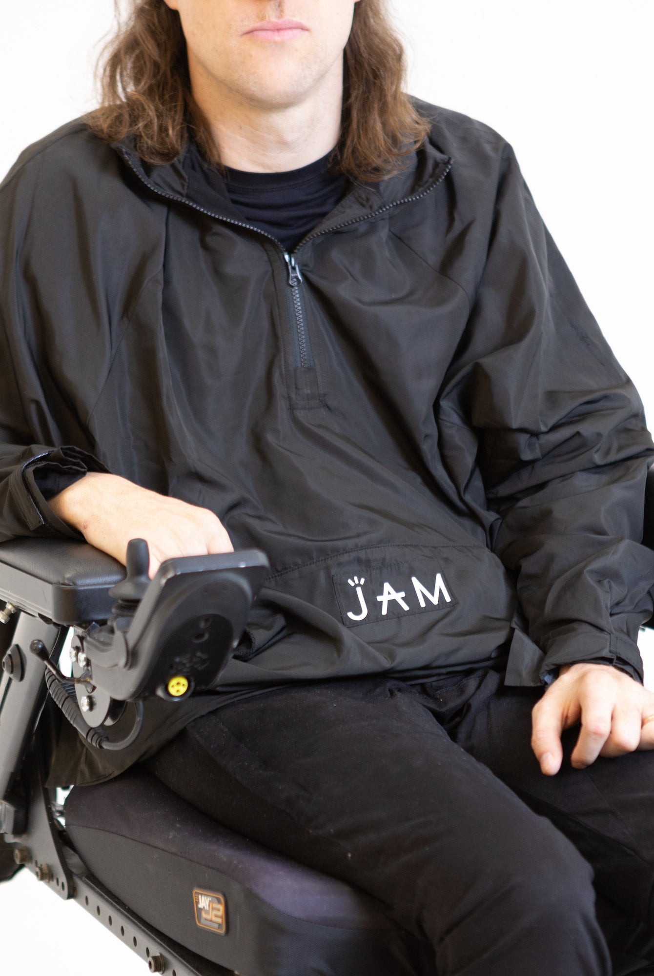 A close up image of a model seated in his wheelchair in front of a white background. He is wearing a black windbreaker jacket with black chinos. #Seated