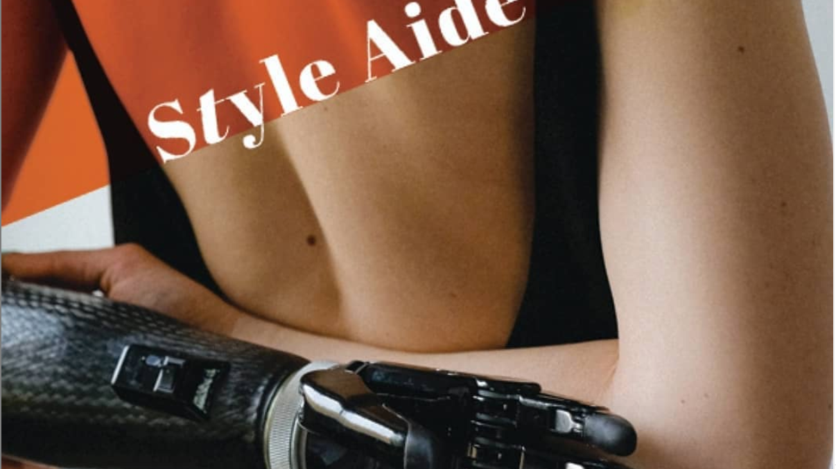 A close up image of a woman's back. The woman has a prosthetic arm. Over the top left is a red corner with the words "Style Aide" in white