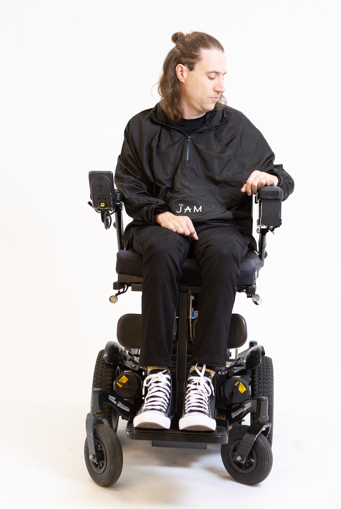 A model seated in his wheelchair in front of a white background. He is wearing a black jacket with black chinos and sneakers. #Seated