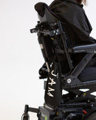 A model seated in his wheelchair visible fro the shoulders down, facing side on to the camera. There is a black drawstring bag with the word "JAM" written on it in white hanging from his wheelchair. #Seated