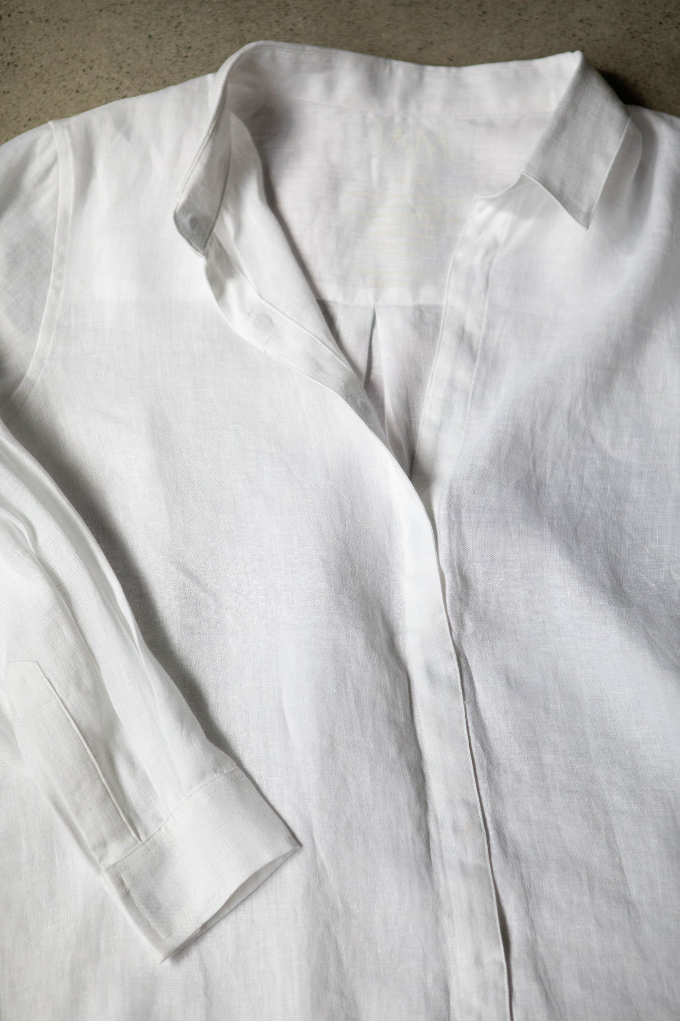 A white linen shirt laying on concrete. The shirt has magnetic closures in lieu of buttons.